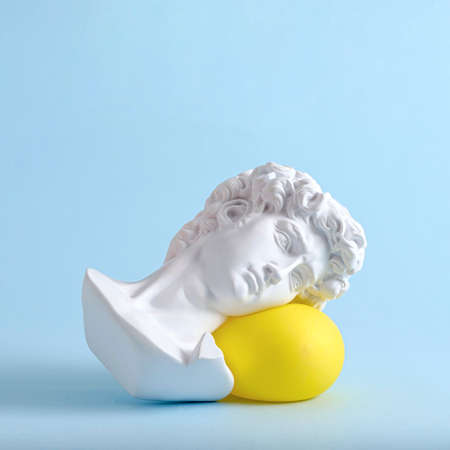 The head and face of David of an antique statue lies on a yellow balloon as a minimal trend concept of vaporwave surreal or sleep.の写真素材