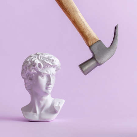 David historical plaster statue of Michelangelo in vaporwave style and a hammer makes a blow. Minimal creative concept on phyllote pastel background.の写真素材