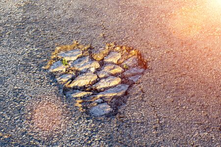 potholes on the asphalt the shape of a heart in the rays of the sun. Texture backgroundの写真素材