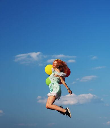 Young redhead girl with colorful balloons jumping at the blue skyの写真素材