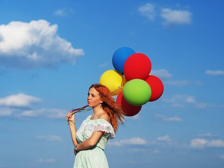 Young redhead girl with colorful balloons standing at the blue skyの写真素材