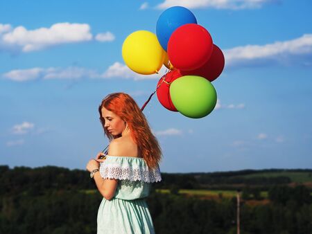 Young redhead girl with colorful balloons standing at the blue skyの写真素材