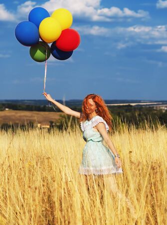 Girl redhead running with ballons at the yellow spikelets and blue skyの写真素材