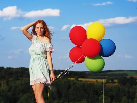 Young redhead girl with colorful balloons standing at the blue skyの写真素材