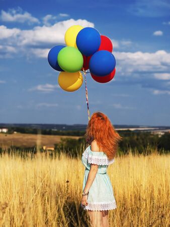 Girl redhead standing with ballons at the yellow spikelets and blue skyの写真素材