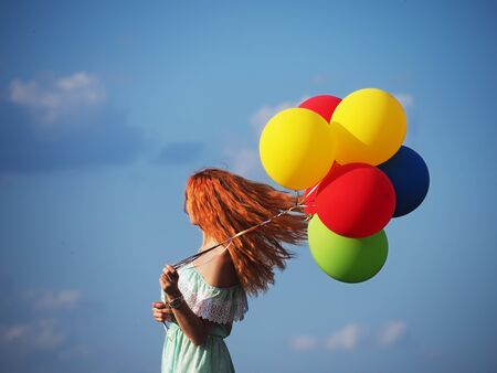 Young redhead girl with colorful balloons standing at the blue skyの写真素材