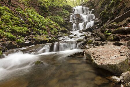 A large boulder lies at the foot of a waterfall in the Carpathian mountainsの写真素材