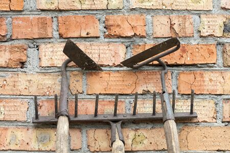 Still life of old / rusty, rake and hoe garden tools against the old weathered brick background making horizontal lines.の写真素材