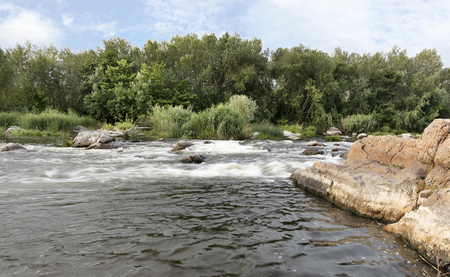 The river Southern Bug in the summer - fast river flow, rocky shores, rapids,bright green vegetation and a cloudy blue skyの写真素材