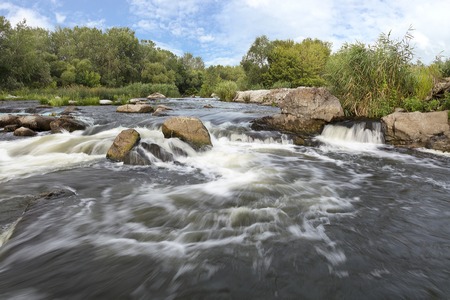 The rapid flow of the river, rocky shores, rapids, bright green vegetation and a cloudy blue sky in the summer. Southern Bug. Ukraineの写真素材