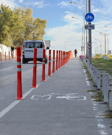 bike path in the park with busy traffic fenced with red road columns against the blue sky and the setting sunの写真素材