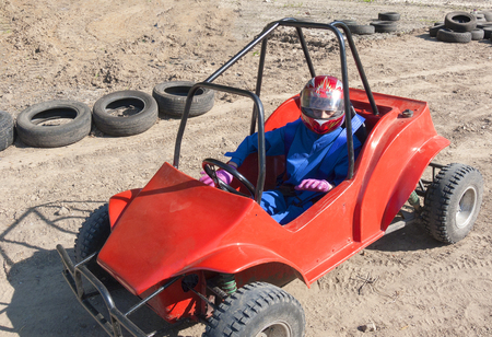 Race of a teenager on a children's buggy kicking up trail of dust on sand trackの写真素材