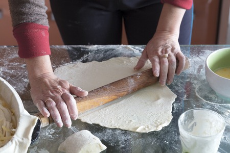 Female hands roll the dough on a glass table to make a cake with cottage cheese.の写真素材