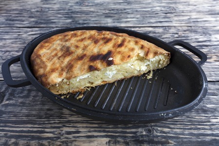Homemade cake with cottage cheese and Parmesan cheese, which melted in a hot oven. Pie on a cast iron plate on an old wooden background.の写真素材
