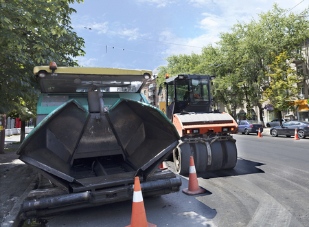 Among the summer noon, a heavy asphalt paver and road vibrating roller compactor is ready to repair a road in a modern cityの写真素材