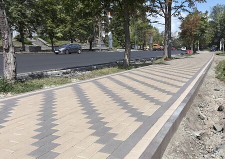 The pedestrian walkway of the city is paved with a new paving slab. The final stage of repair of the road and sidewalks of the city street is coming to the end.の写真素材
