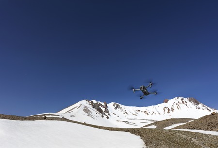 The quadrocopter flies against the backdrop of Mount Ercyes on a clear sunny day amidst a blue clear sky in central Anatolia, Turkey.の写真素材