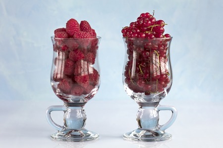 Raspberry and red currant poured into transparent glass cups for latte and stand in a row on a light...