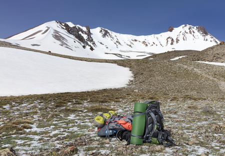 Backpacks of tourists are located at the foot of the mountain against a clear blue skyの写真素材