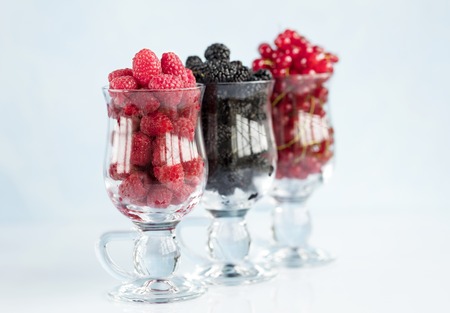 Raspberry, a big black blackberry and red currant are poured into transparent glass cups for latte...