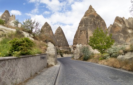 A winding road from paving stones passes near the stone cone houses in the ancient rocks of Goreme, Kappadoki. Rural landscape in the rural way of life of old mountain formations.の写真素材