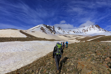 A group of tourists with backpacks behind their backs goes hiking on a rocky slope to the snow mountain Erciyas in Turkeyの写真素材