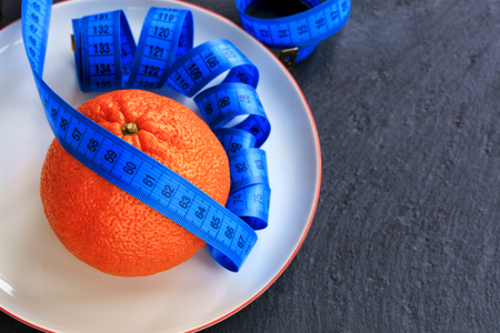 Orange ripe mandarin and meter lie on a white porcelain plate, the concept of a healthy diet for weight loss.の写真素材
