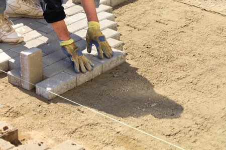 The worker puts the paving slabs along the stretched thread on the prepared flat sandy ground on the sidewalk.の写真素材