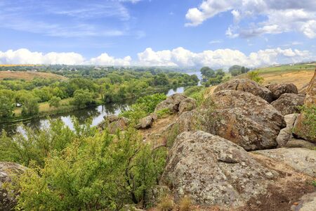 The Southern Bug River in the summer is rocky shores, bright green vegetation and a cloudy blue sky.の写真素材
