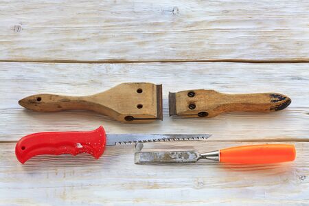 Old carpentry tools, cycles, hand saw and chisel lie on a white wooden table.