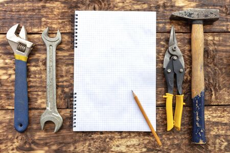 Old hand tools, hammer, metal shears, adjustable wrench, carob wrench surround an empty notebook...