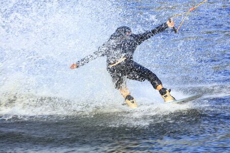 A wakeboarder rushes through the water at high speed creating a cloud of spray around himself.