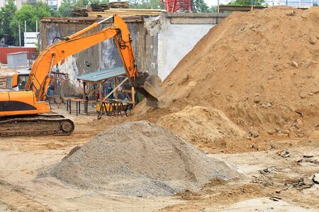 Heavy crawler construction excavator loads sand at a construction site during road repair on a city...