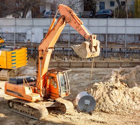 A heavy crawler construction excavator lifts and carries a large mortar mixer for laying concrete piles in the foundation of the future home, image with copy space.の写真素材