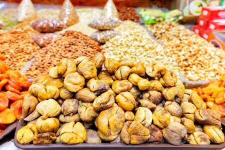 Slides with dried ugly figs, dried apricots on a background of various nuts in blurry form are sold on the shelves of the eastern market.の写真素材