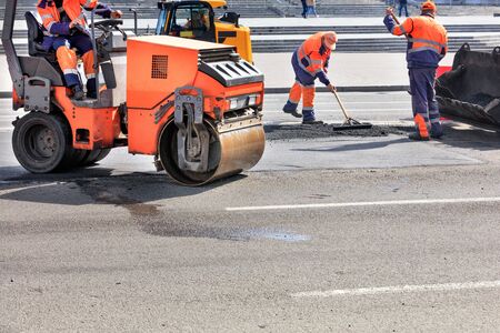 Road service workers use a vibratory roller, a road bulldozer and a metal level to repair the...