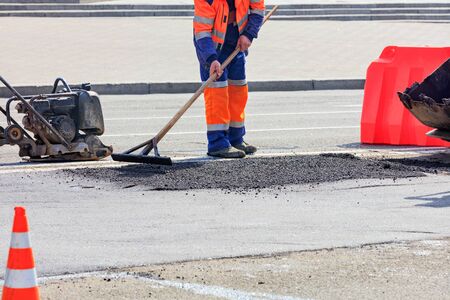 The road builder levels the fresh asphalt with a wooden level in road repair against the background of a vibrating plate and part of the bucket of a road bulldozer.の写真素材