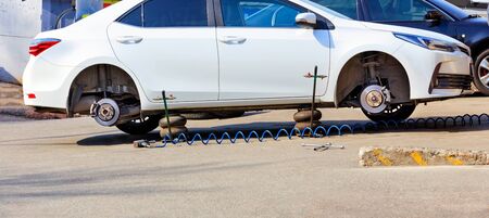 A white car without wheels stands on air jacks at a service station to replace tires.