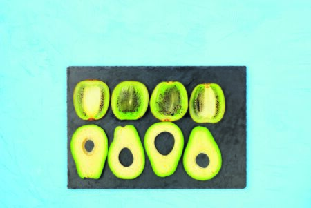 Ripe slices of kiwi and avocado are neatly laid out in a row on a gray stone, delicious and...