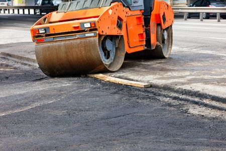 The metal cylinders of a large vibratory roller roll onto a new section of the road surface for...