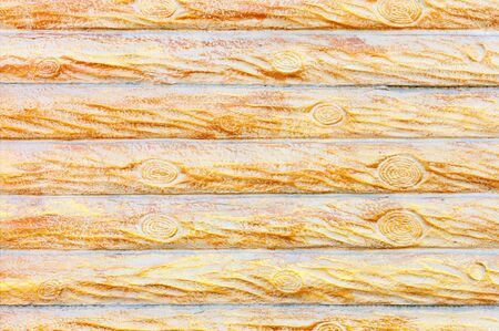 The texture and background of the concrete wall under a stylized wooden fence in the form of horizontal logs in yellow-gold color.の写真素材