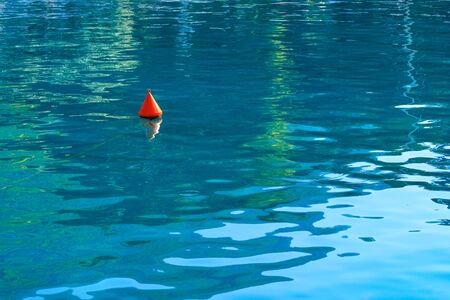 An orange buoy on the turquoise sea waves shows the direction of movement for marine boats and boats and a safe area for them.の写真素材