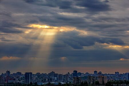 The sun's rays break through dense clouds at dawn over a sleeping city. Shining light in the...