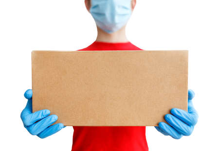 Courier delivery service with a cardboard box in hands. A man in a medical mask and rubber gloves,...