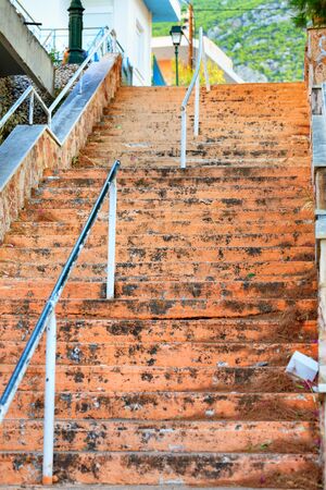 The shabby steps of an old stone staircase rise uphill and lead to the light under the bright sun on a narrow Greek street, selective focus.の写真素材