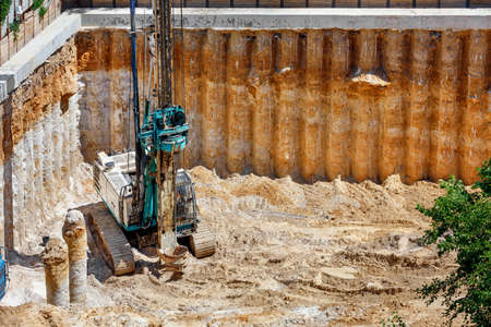 A large excavator installs concrete columns of drilling rig to strengthen the foundation of the future high-rise building, a viewing angle from a height, copy space.の素材 [FY310150614060]