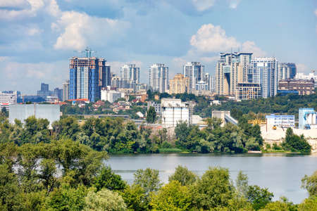 Construction of new high-rise buildings on the right bank of the Dnipro River in Kyiv, a view of the facades of multi-storey residential buildings among private houses and a blue cloudy sky, copy space.の写真素材