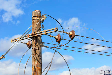 The top of an old concrete pillar with electric wires and a connected three-phase current stands...