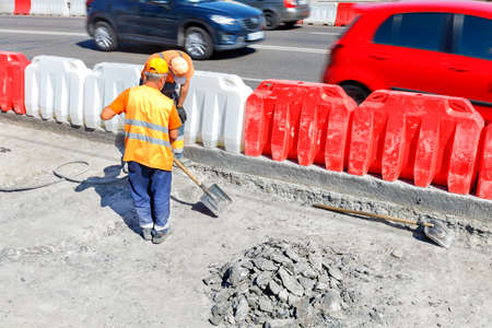 Road workers repair an old section of road with a pneumatic jackhammer and shovel, removing worn out...