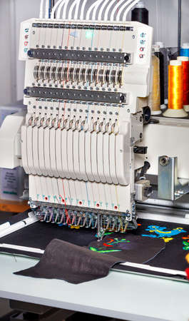 Modern professional embroidery machine for embroidery on various fabrics and leather with multi-colored spools of thread in a blur, vertical image, space for text.の写真素材
